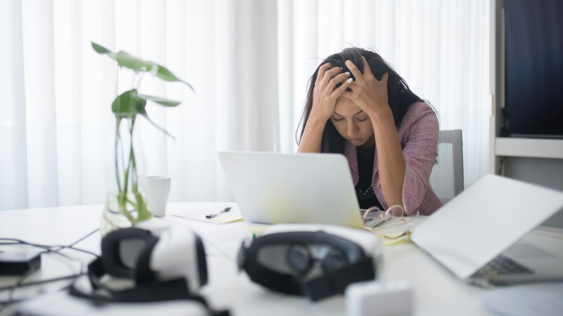 Frustrated woman sitting at desk with laptop, showing stress in a modern office environment.