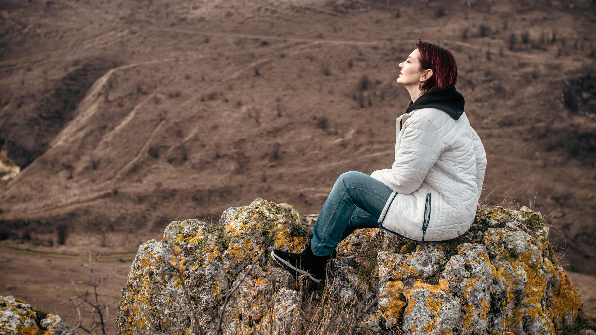 Woman enjoying solitude on a rocky mountain peak, eyes closed in leisure.