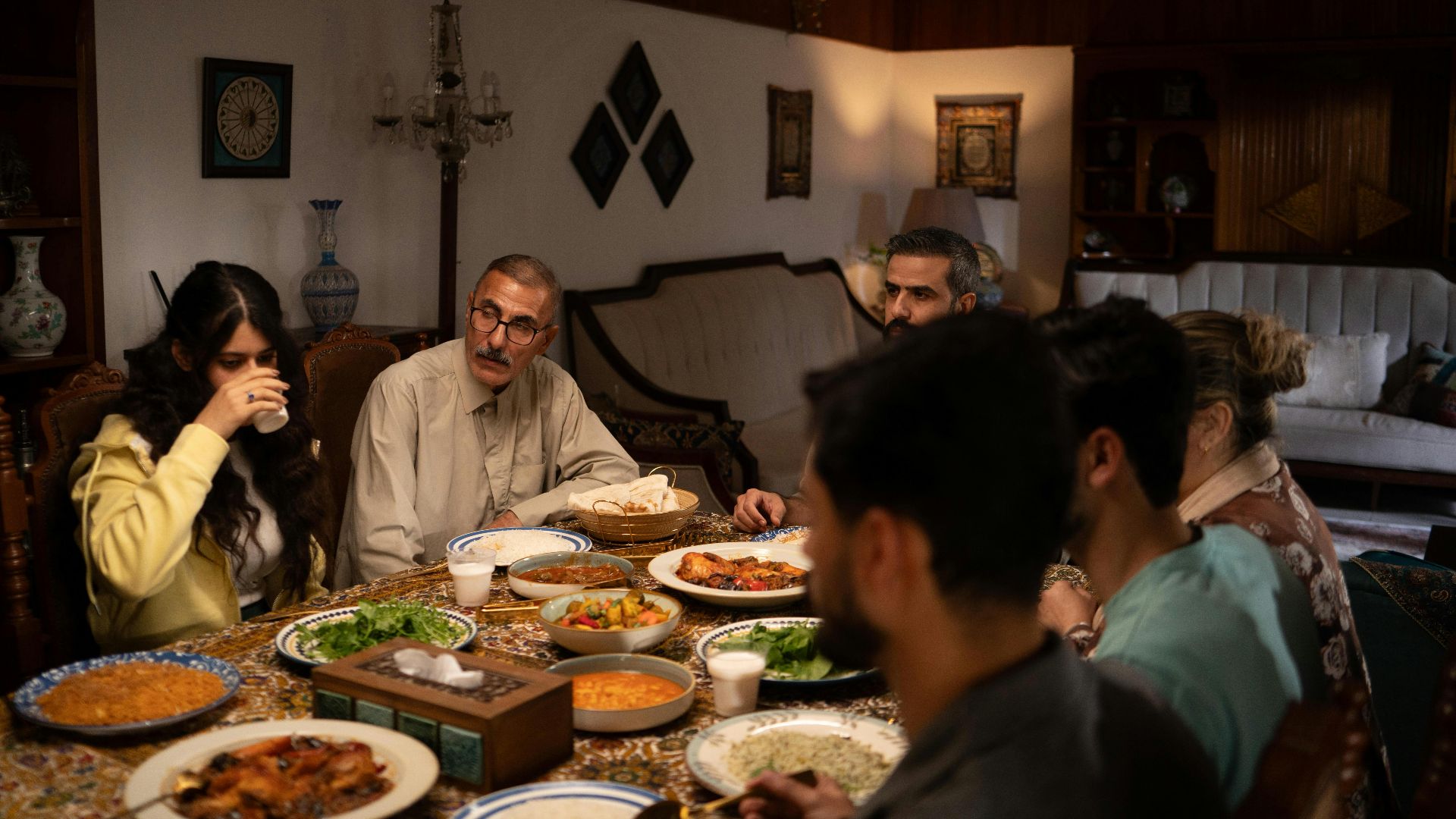 A family enjoys a traditional meal around a dining table in a warmly lit living room.