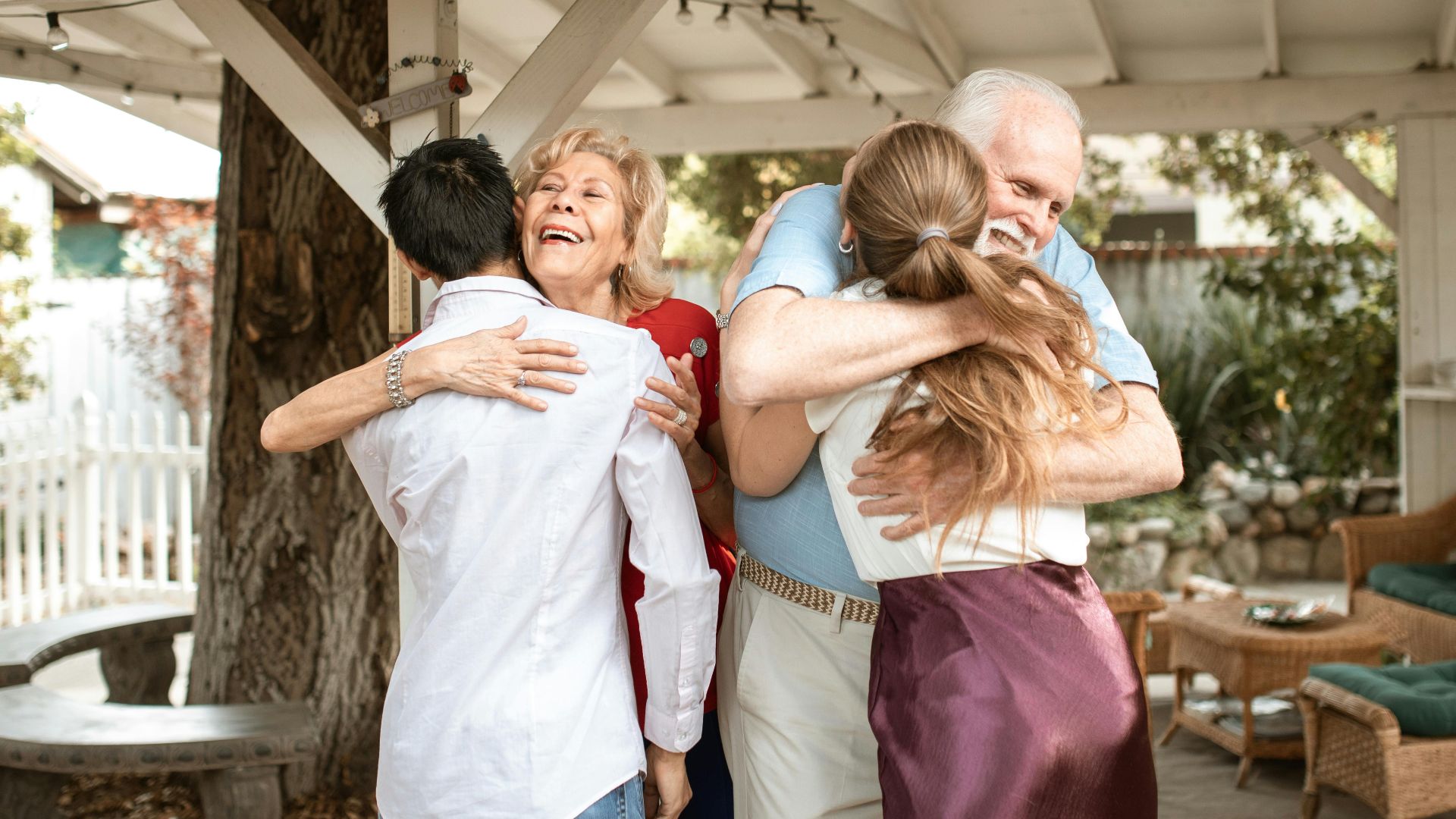 A joyful family reunion outdoors with warm hugs and smiles under a wooden pergola.