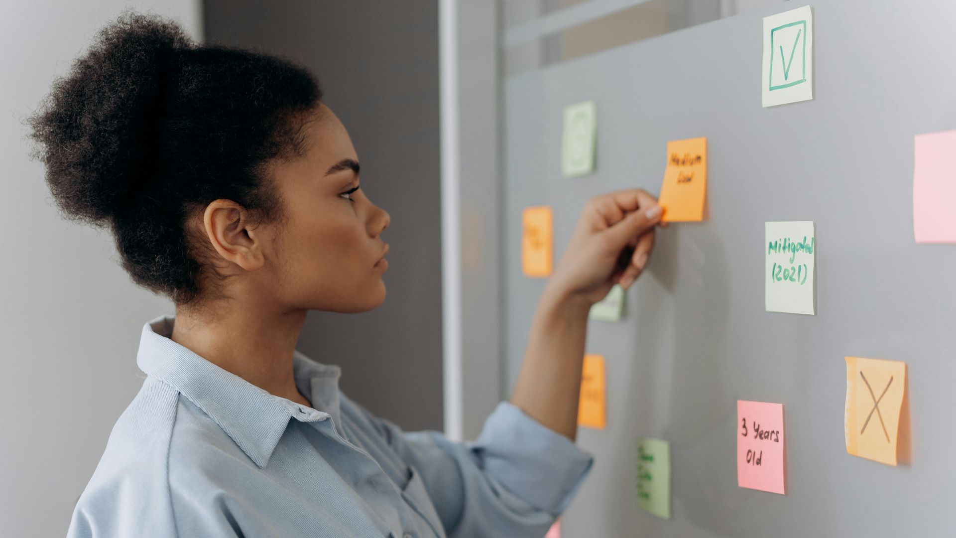 Side view of a young woman organizing colorful sticky notes on a whiteboard.