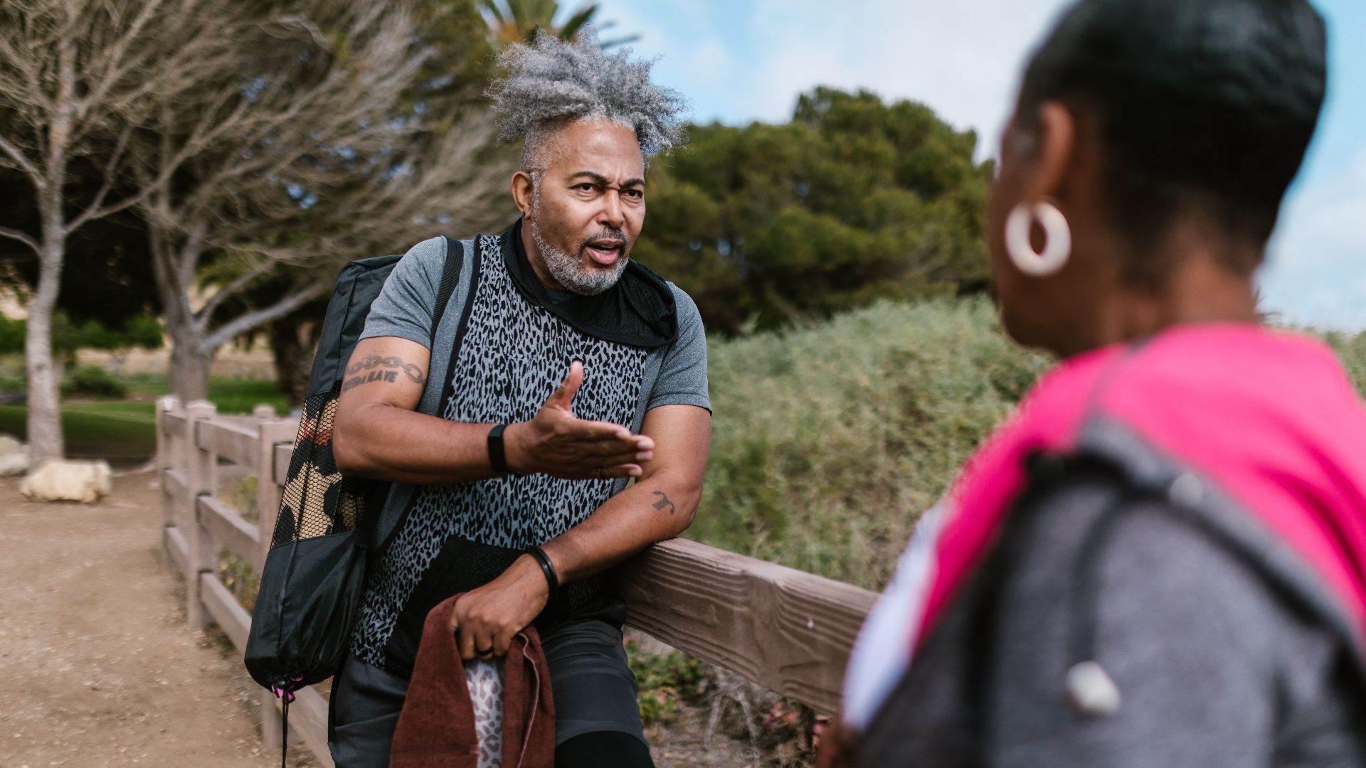 Two adults engage in a lively conversation outdoors by a wooden railing.