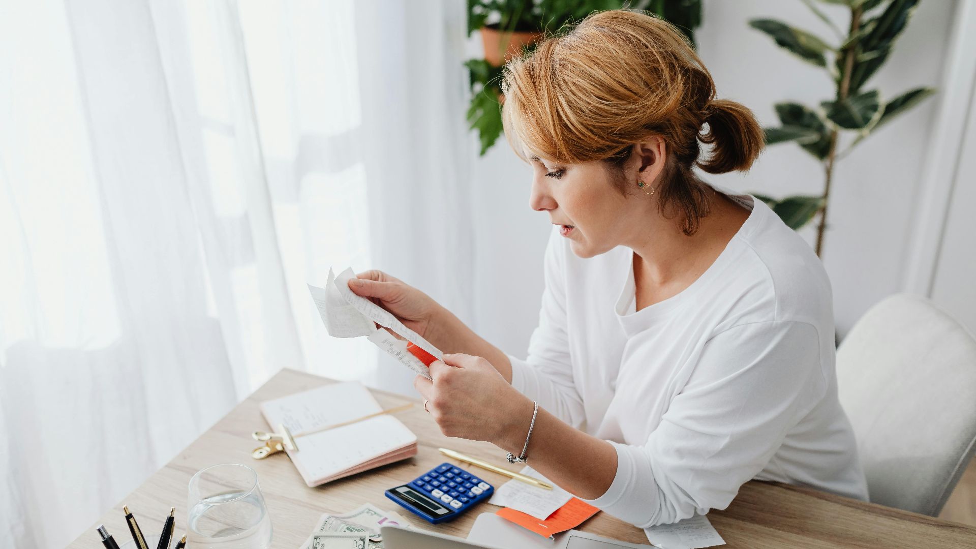 Woman sitting at a desk managing finances with a calculator and paper receipts in an office setting.