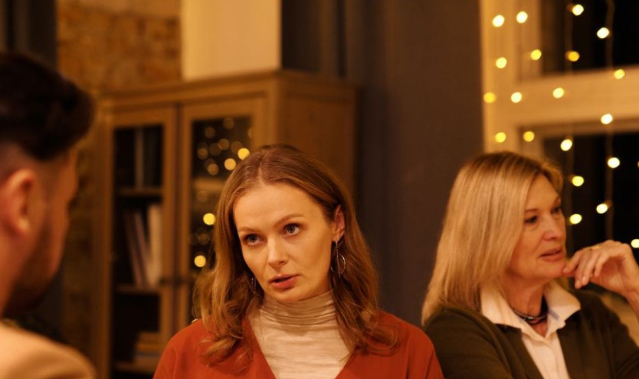Three people enjoying a festive dinner table conversation surrounded by warm holiday lights