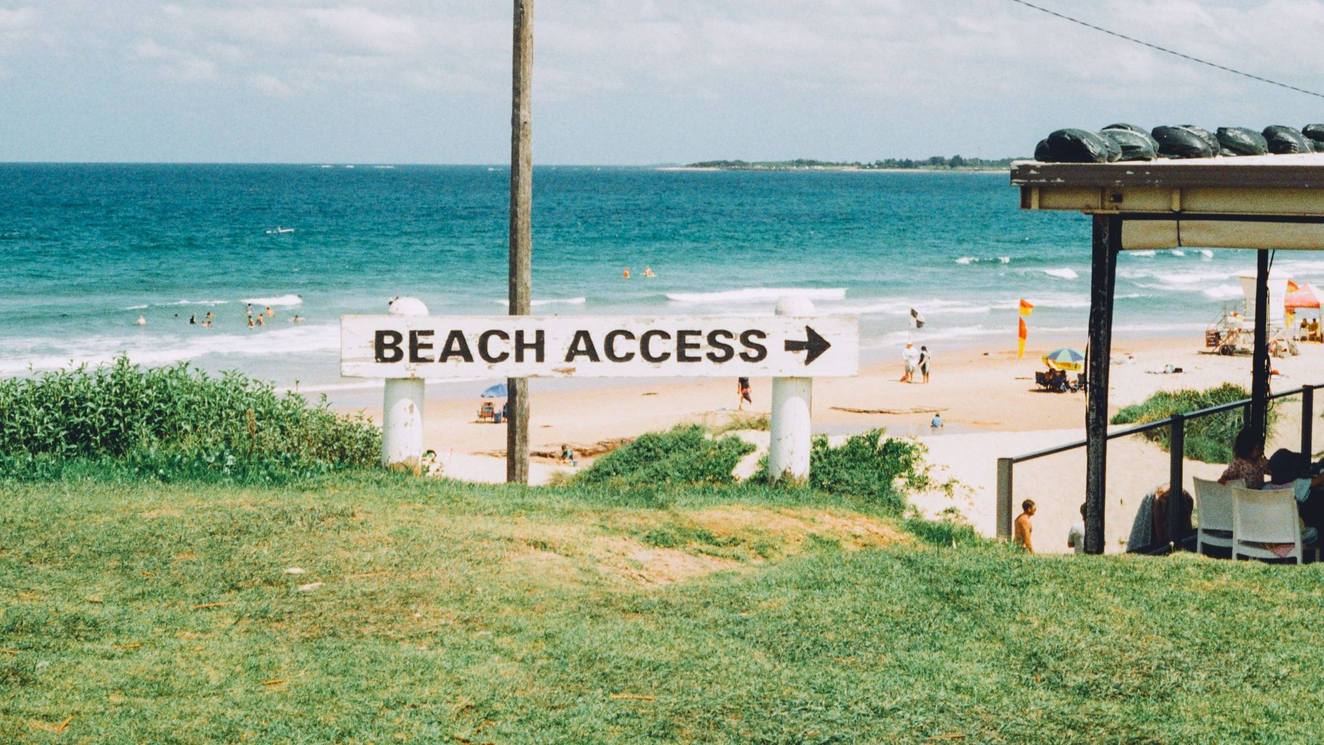A scenic view of a beach access sign pointing towards the sandy shores at Wollongong, NSW, Australia.