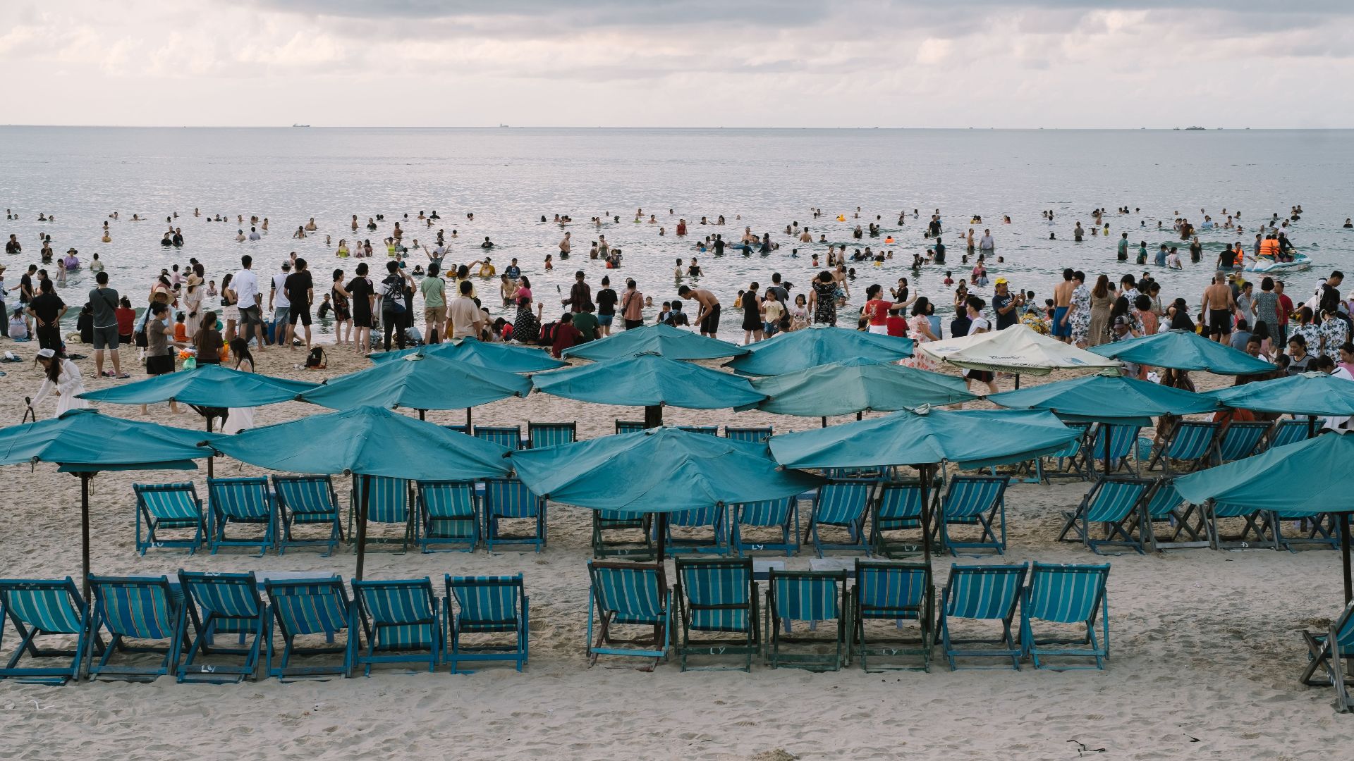 A lively beach scene with blue umbrellas, chairs, and people enjoying the sea.