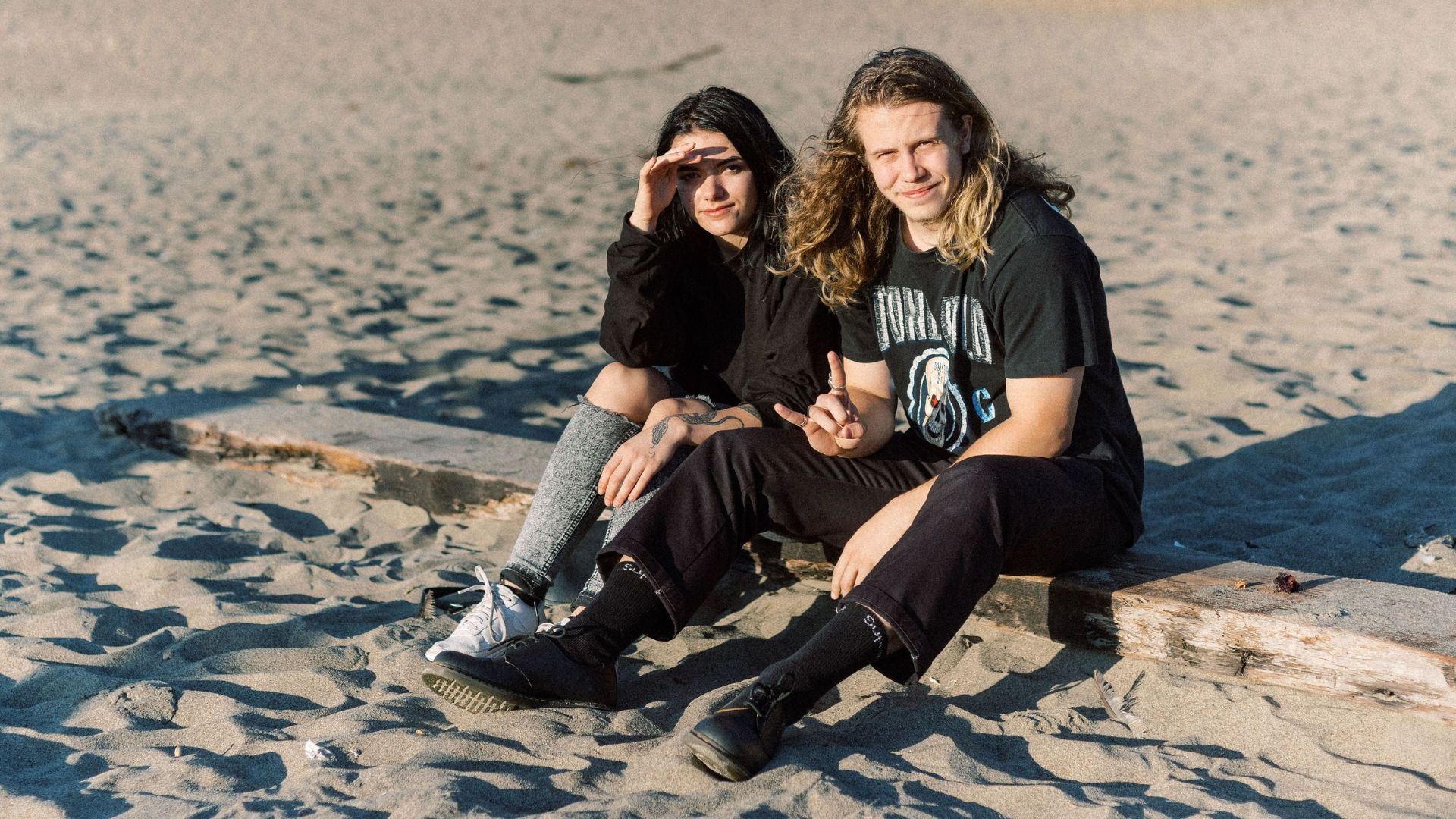 A young couple enjoys the sunny beach with rocky cliffs in the background.