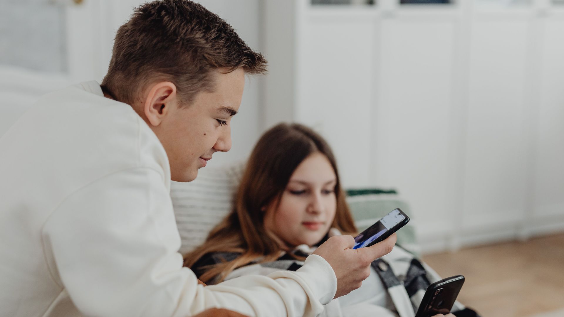 Two teenagers using smartphones in a cozy indoor setting, focused and relaxed.