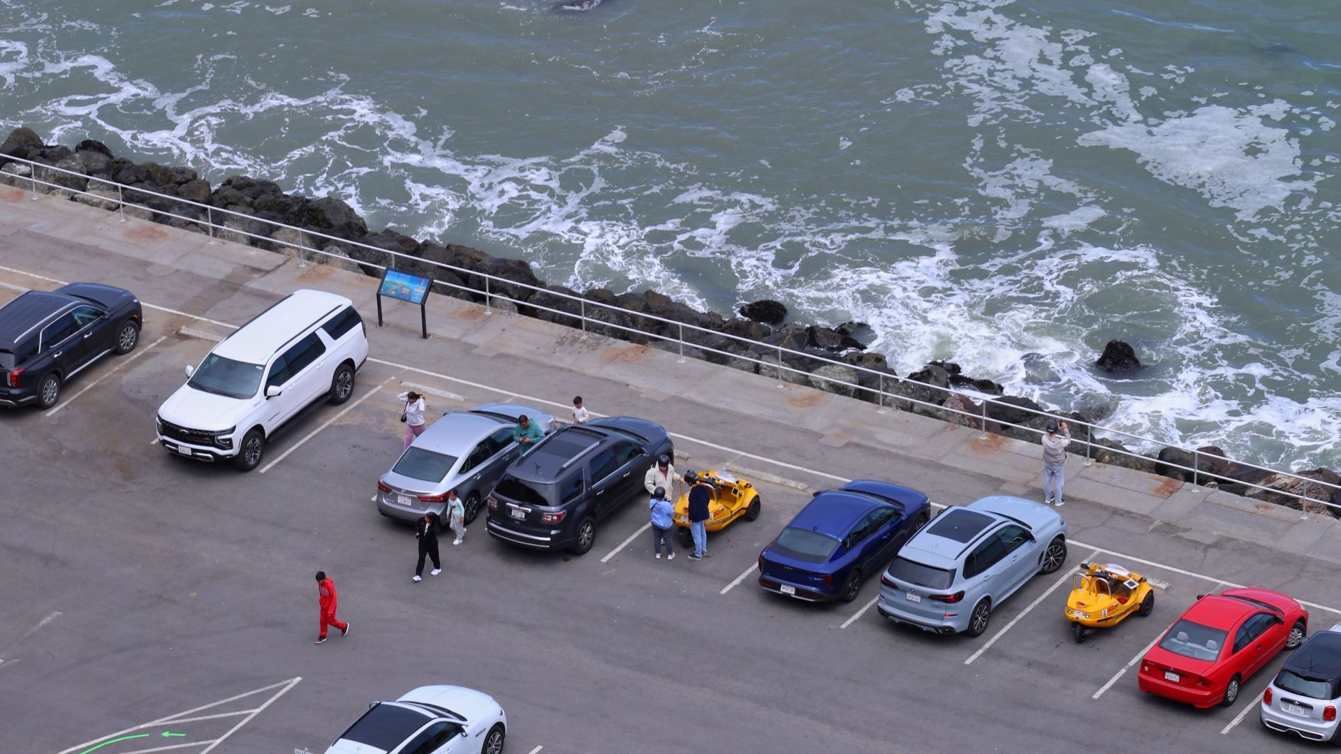 An aerial view showcasing a beachfront parking area in San Francisco with waves and parked cars.