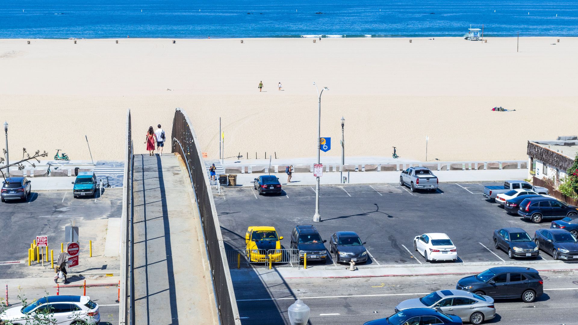 Aerial view of a coastal parking lot with footbridge leading to a serene beach.