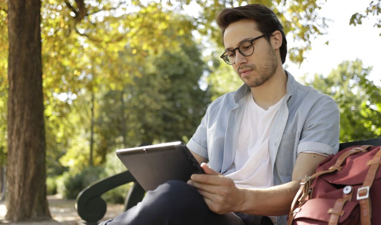 Relaxed young man reading a tablet outdoors in a sunny park setting