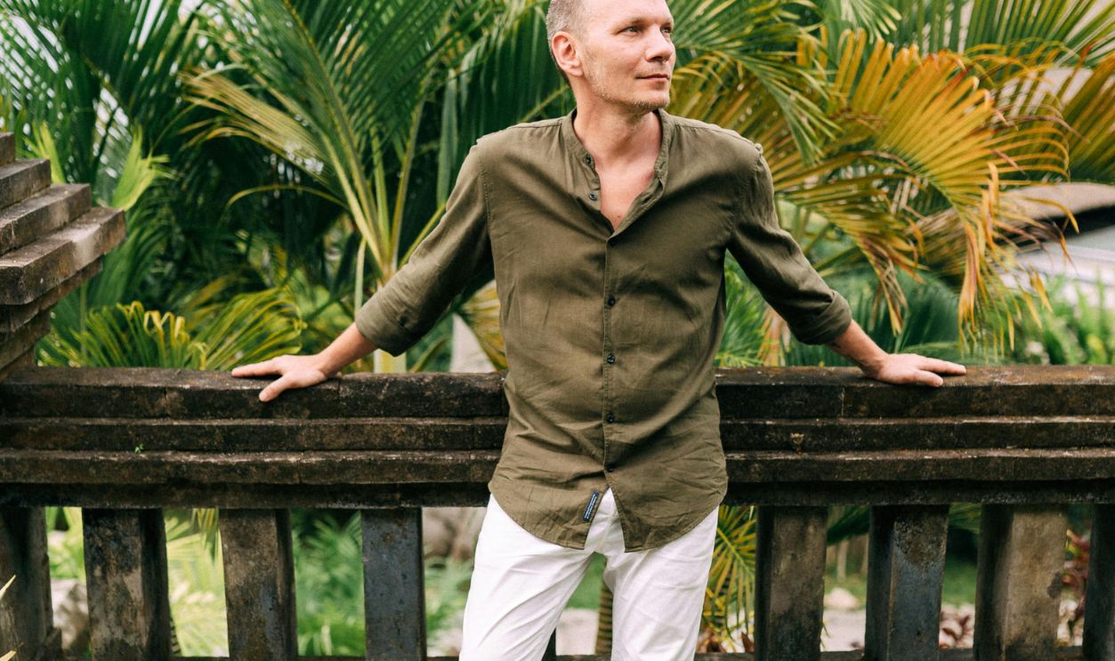 Man standing barefoot in a lush garden, leaning on a fence, enjoying the tropical surroundings