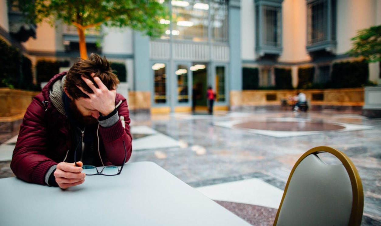 Man holding eyeglasses in hand, showing stress in a modern indoor atrium