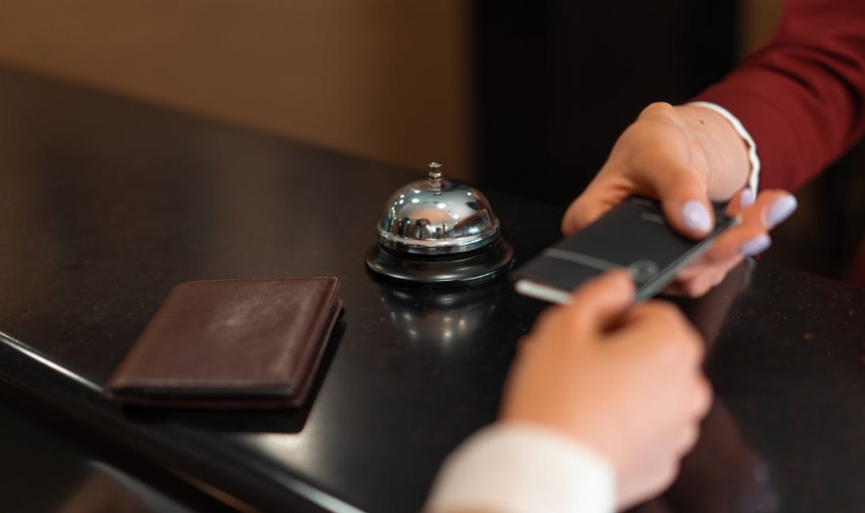A close-up of a hotel check-in process with a smartphone and card transaction at the reception desk.