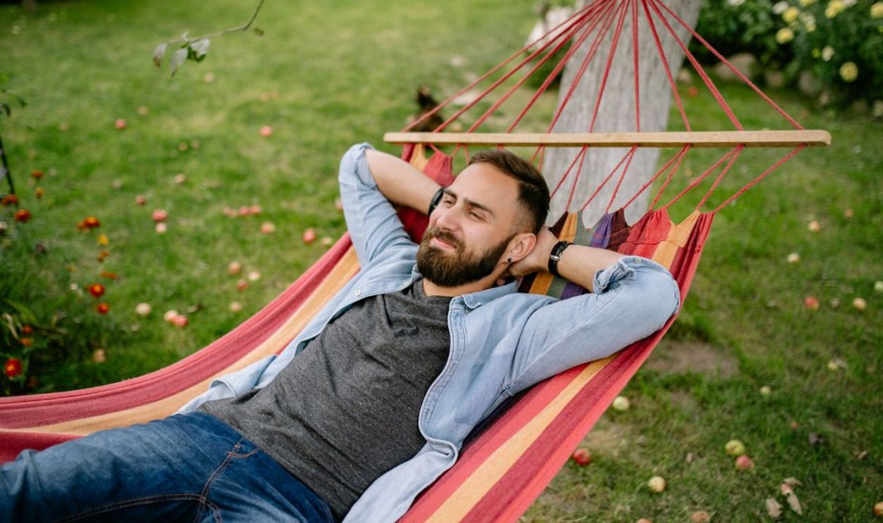 Bearded man in denim shirt enjoying a sunny day lying in a hammock in the garden