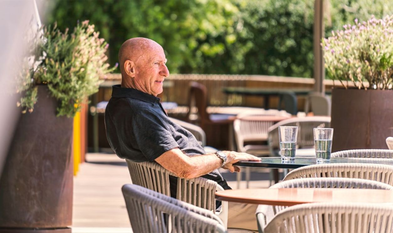 Senior man sitting at an outdoor patio, enjoying a sunny day with drinks on the table