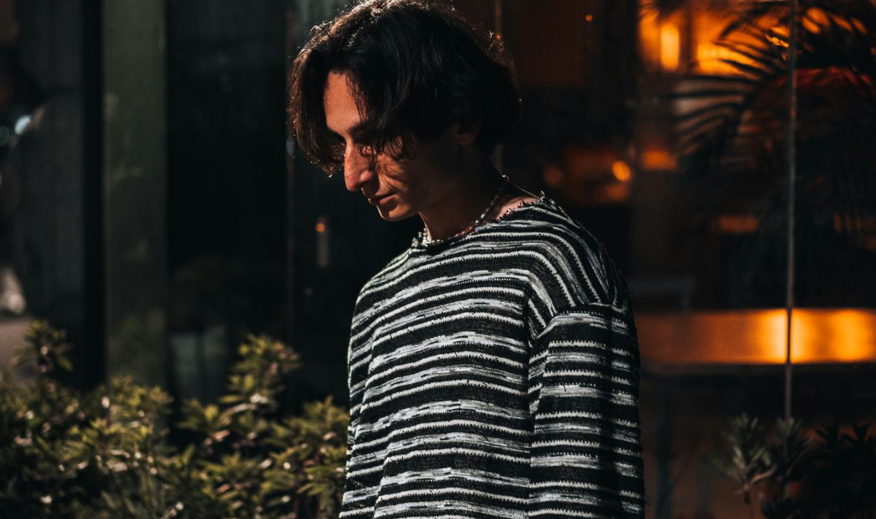 Portrait of a man standing with hands in pockets, illuminated by street lights at night.