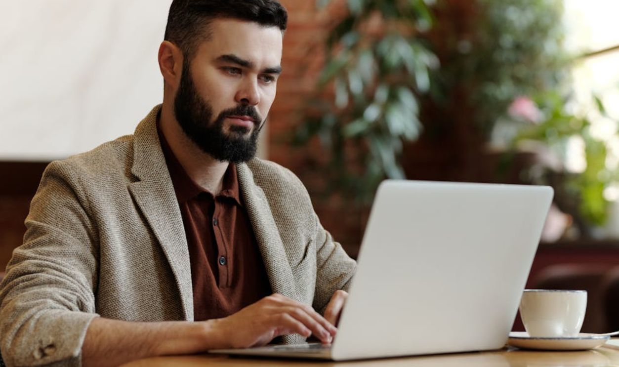 Businessman working on laptop in a cafe setting, surrounded by plants, sipping coffee.