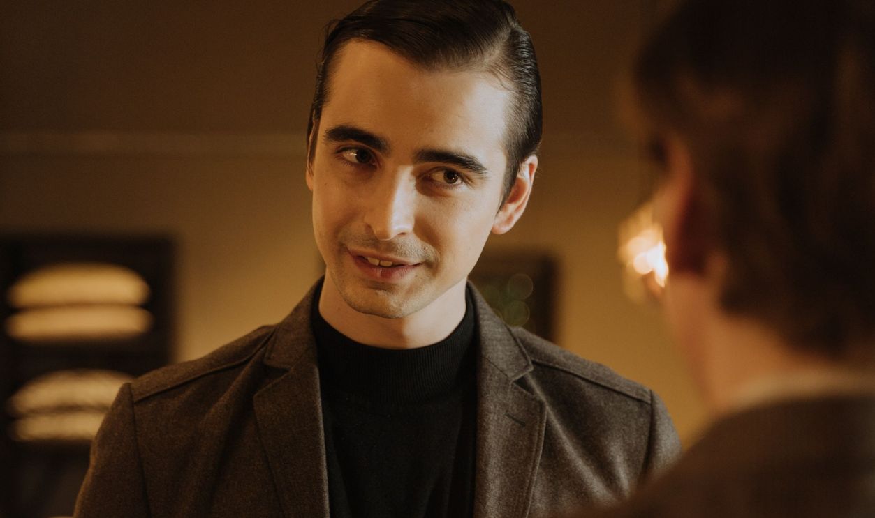 Young adult man in a suit conversing in a warmly lit indoor setting.