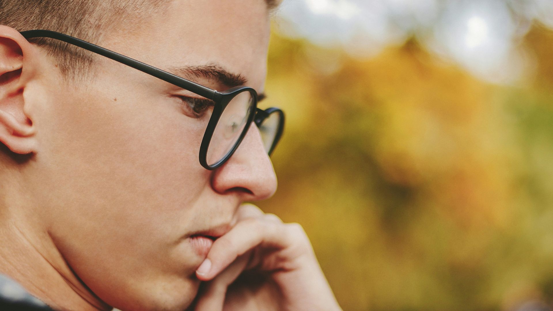 boy with black framed eyeglasses holding face