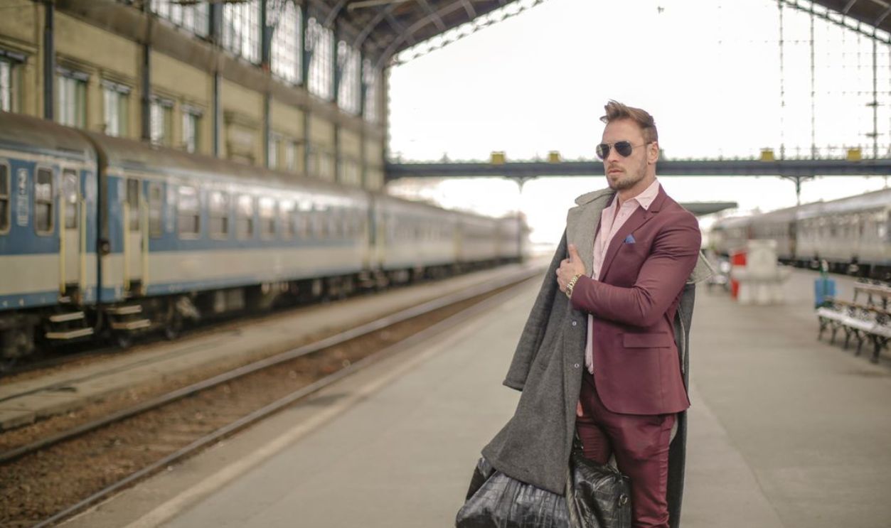 Stylish man in maroon suit and sunglasses waiting at a historic railway station