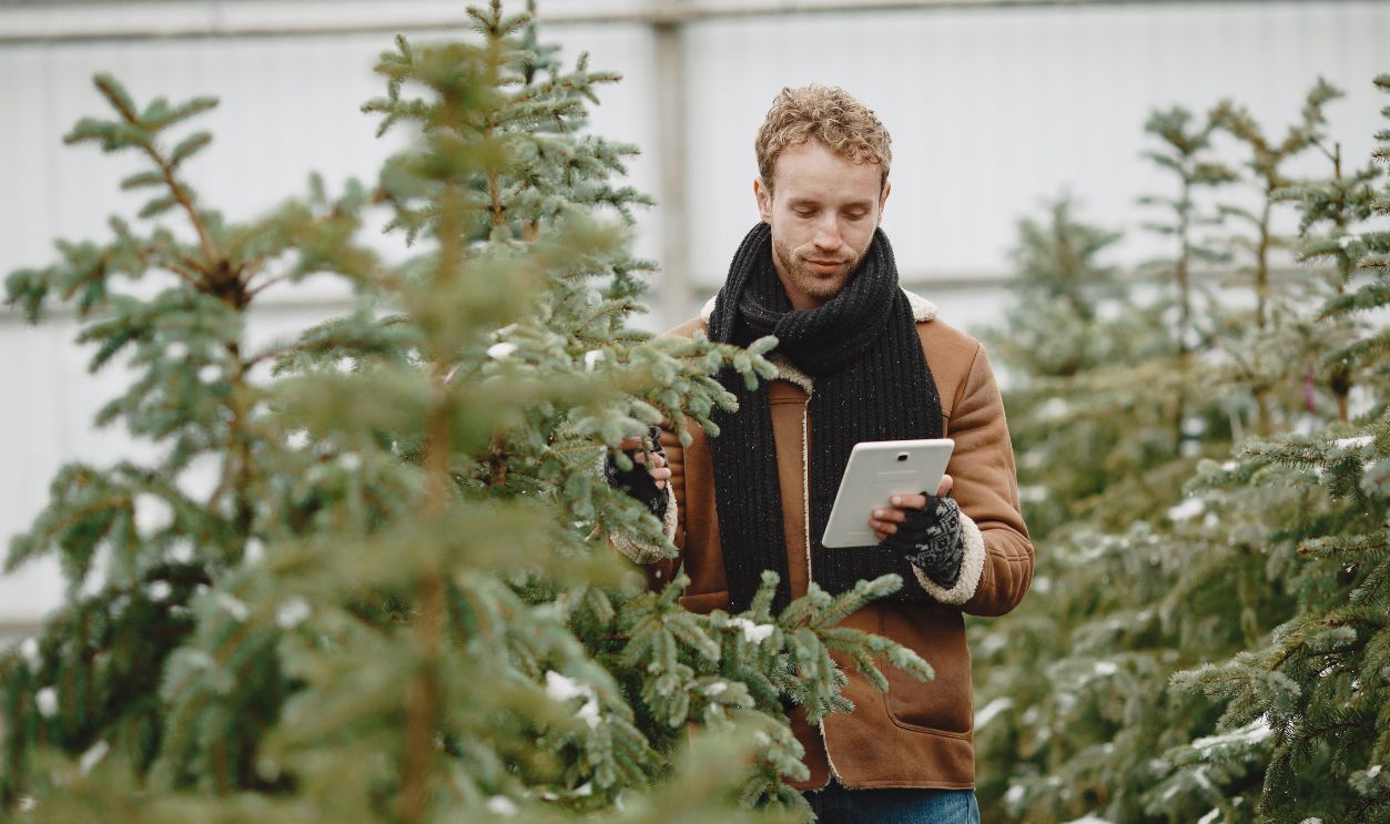 Caucasian man in winter attire using a digital tablet among snow-dusted trees in a nursery