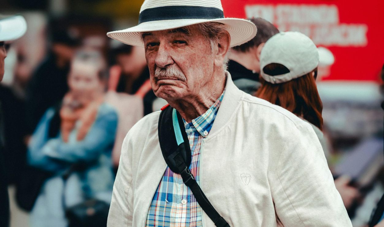 Portrait of senior man wearing a hat at an outdoor gathering, showing emotion