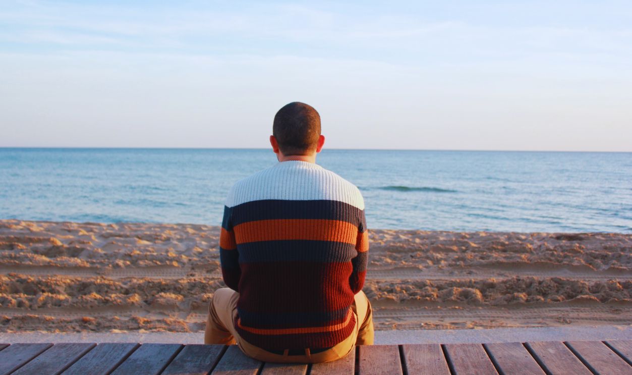 A man sitting on a wooden pier overlooking the tranquil ocean horizon
