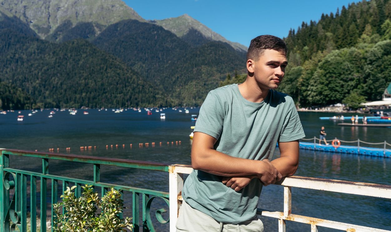 Young man enjoying a peaceful moment by the scenic Lake Ritsa, surrounded by mountains in summer.