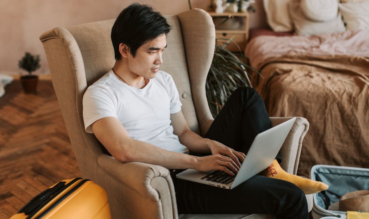 A man sitting comfortably in an armchair, using a laptop in a cozy home interior