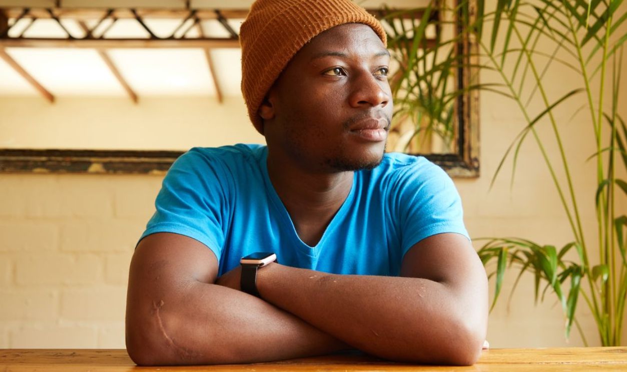 A young man in a beanie sits thoughtfully at a table indoors. Calm and relaxed ambiance.