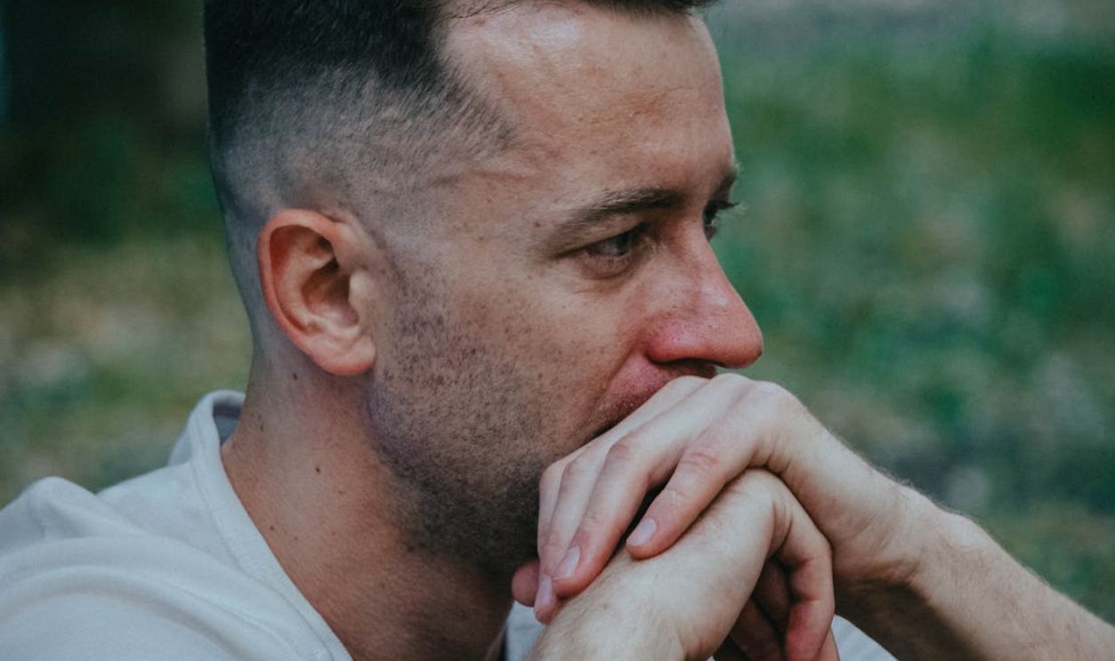 A thoughtful man outdoors, hands clasped near face, reflecting deeply