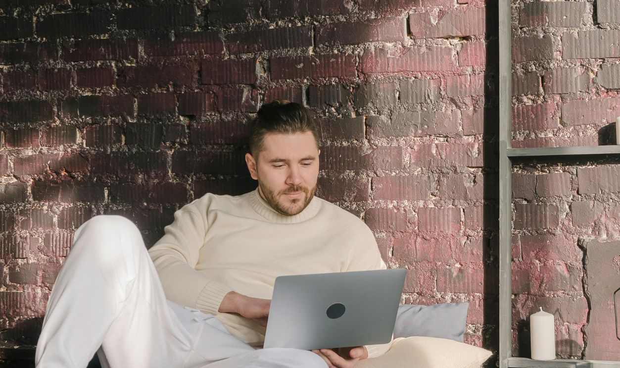 Man comfortably working from bed with a laptop in a stylish, sunlit room