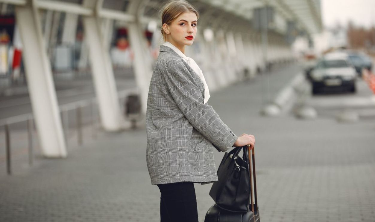 Confident businesswoman standing with luggage outdoors, ready for travel.