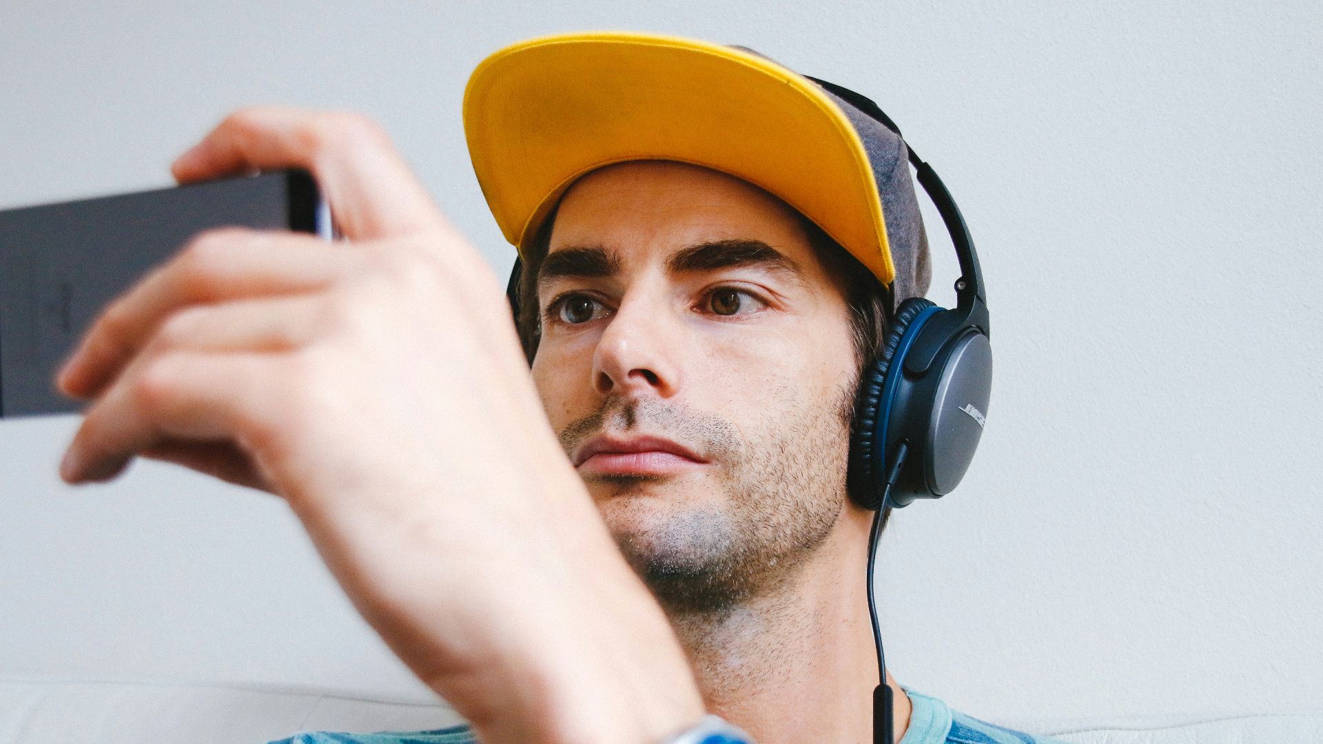 man wearing black corded headphones while holding phone
