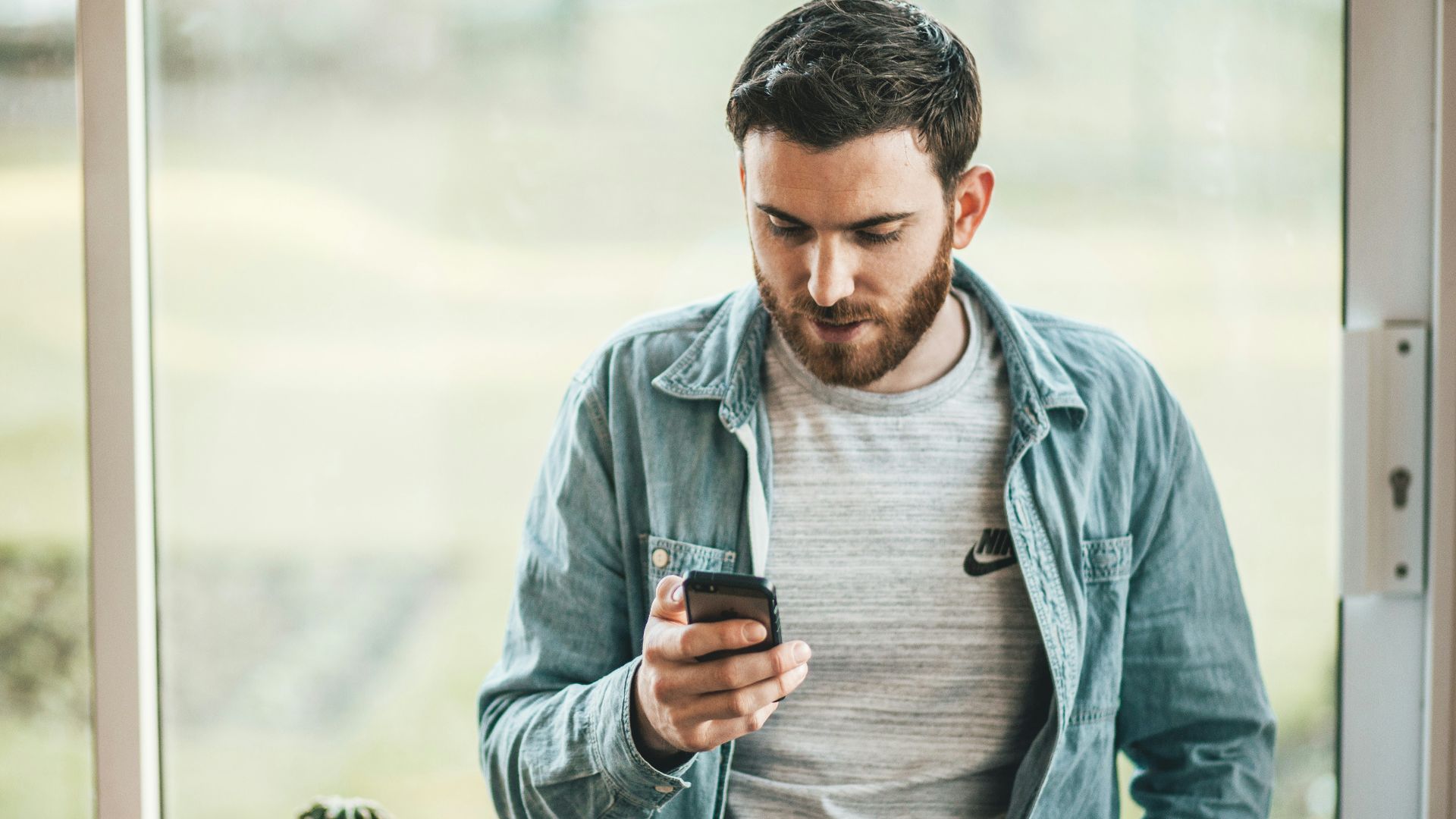 man holding a smartphone near the window