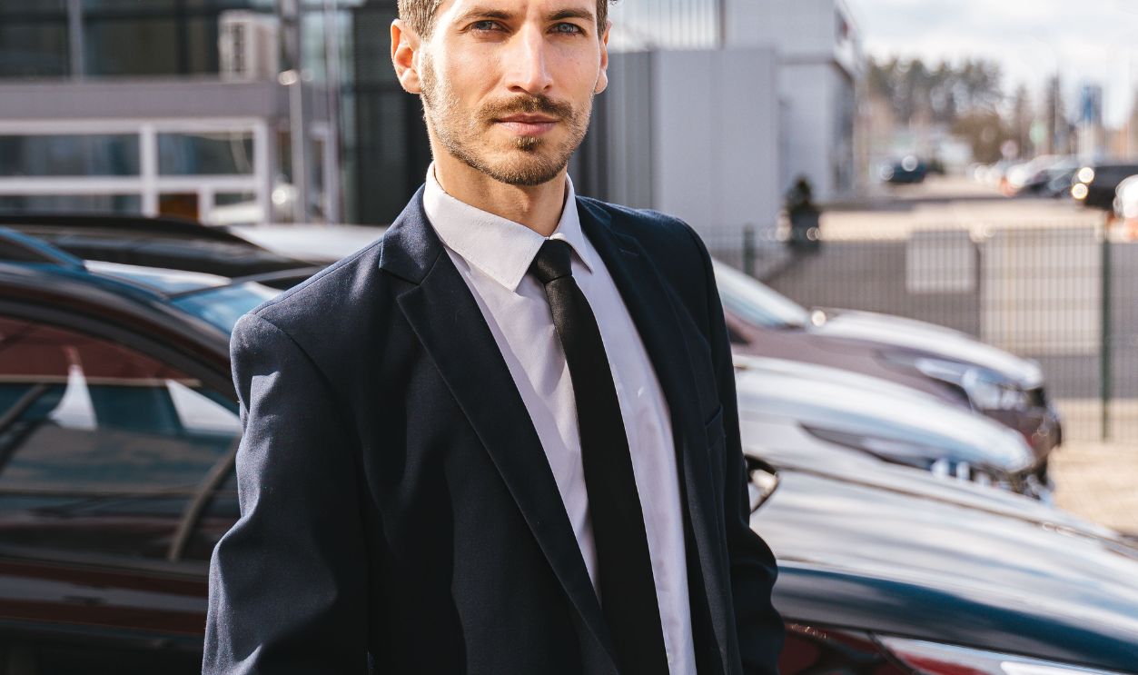 Professional man in a suit standing next to cars outside a modern building