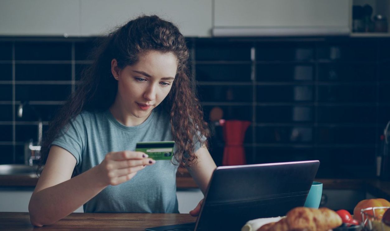 Young woman using a credit card to shop online with a laptop in a kitchen setting