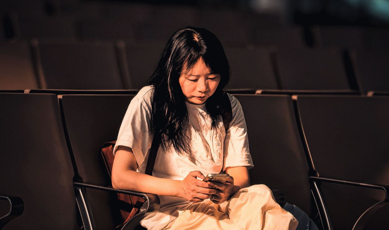 A young woman sits alone in an empty terminal, engrossed in her phone