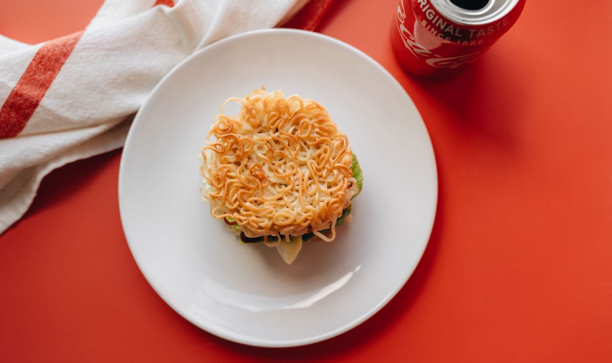 Delicious Ramen burger placed on a white plate with a red backdrop, offering a unique culinary twist.