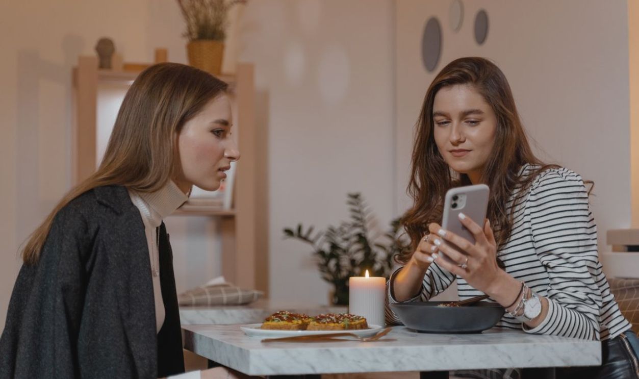 Two women enjoying a cozy indoor setting, with food and smartphone.