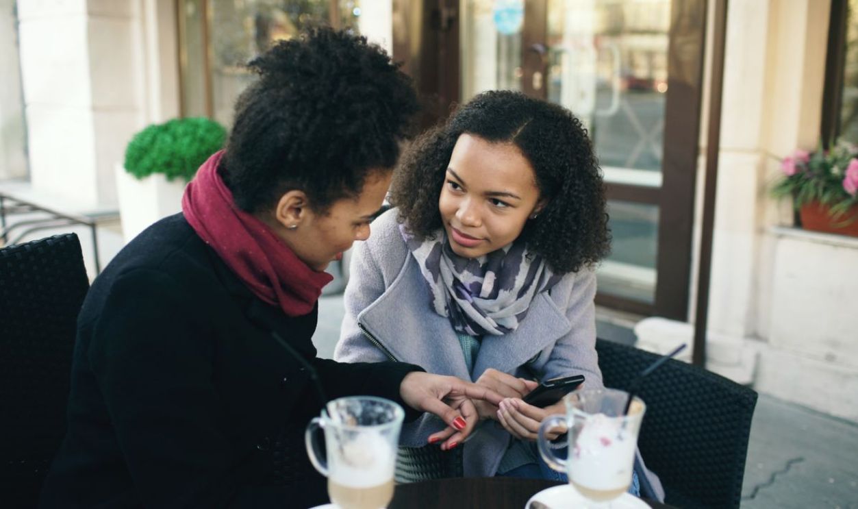 Two women having a conversation over coffee in an outdoor cafe setting.