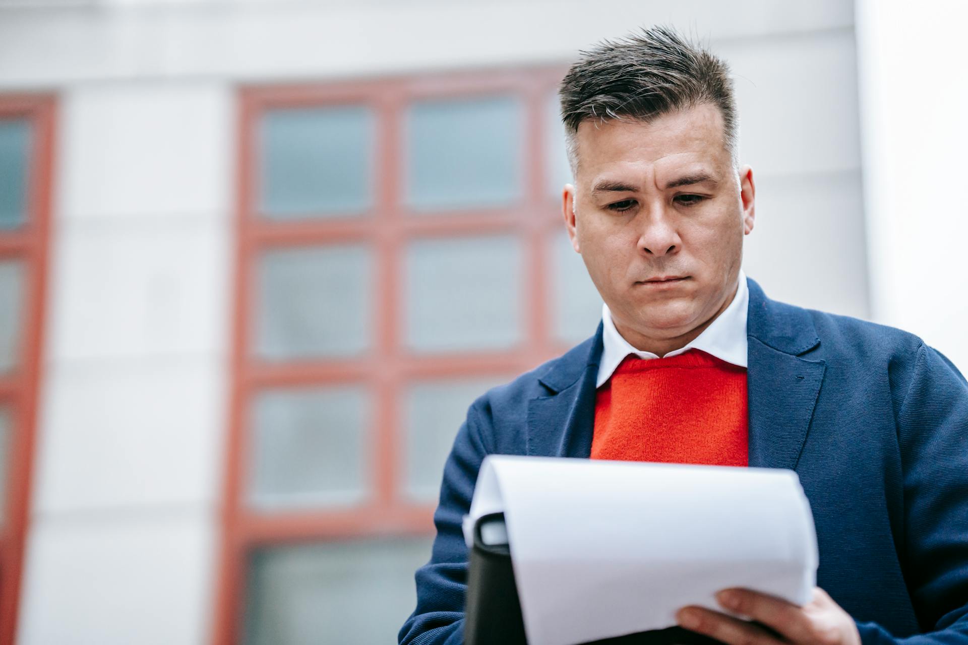 Professional man in smart attire reviewing paperwork outside modern building.