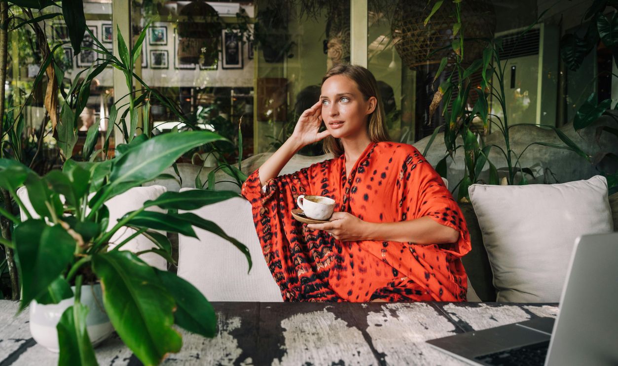 Stylish woman in a red dress holding coffee at a cafe with lush green plants