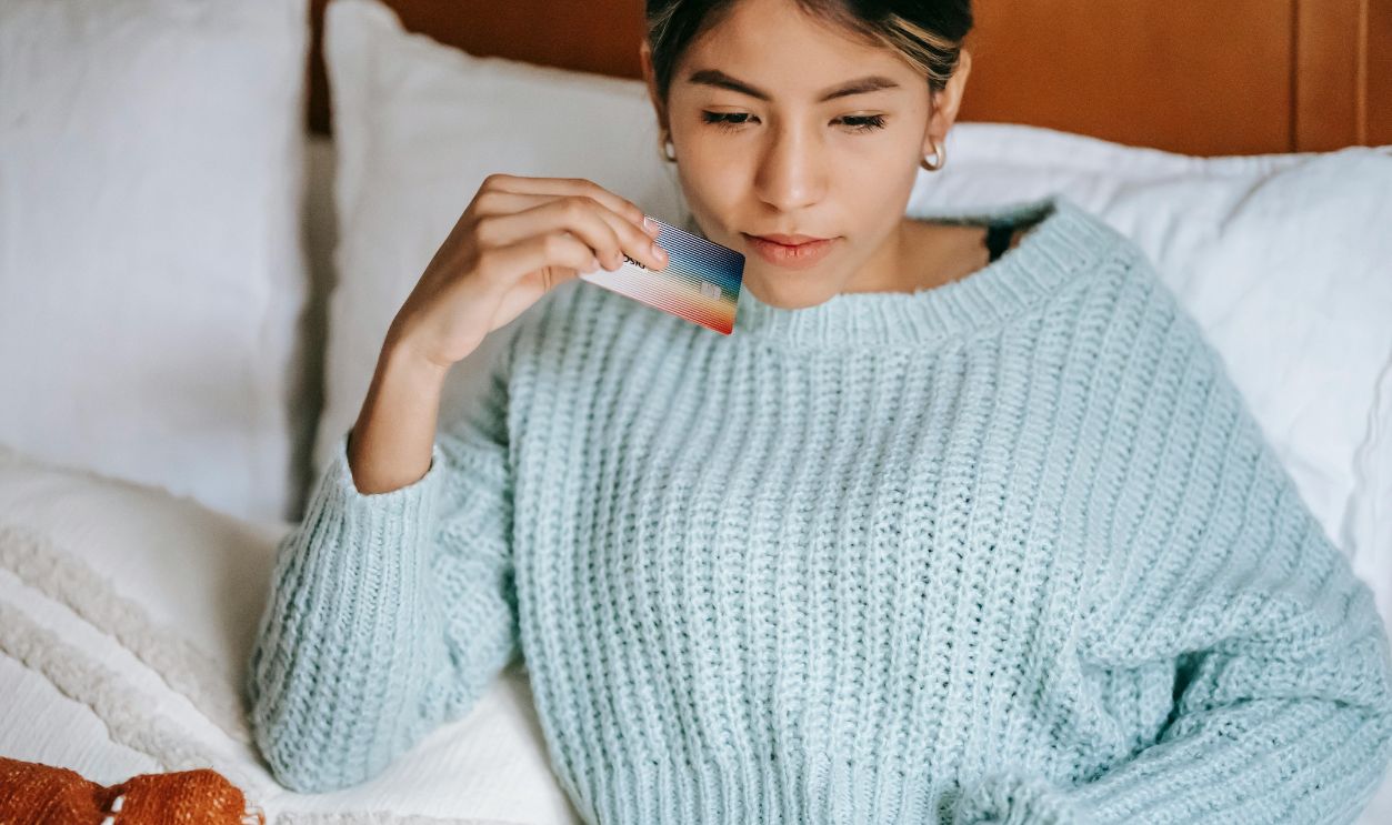 Young woman in a cozy sweater makes an online purchase from the comfort of her bedroom
