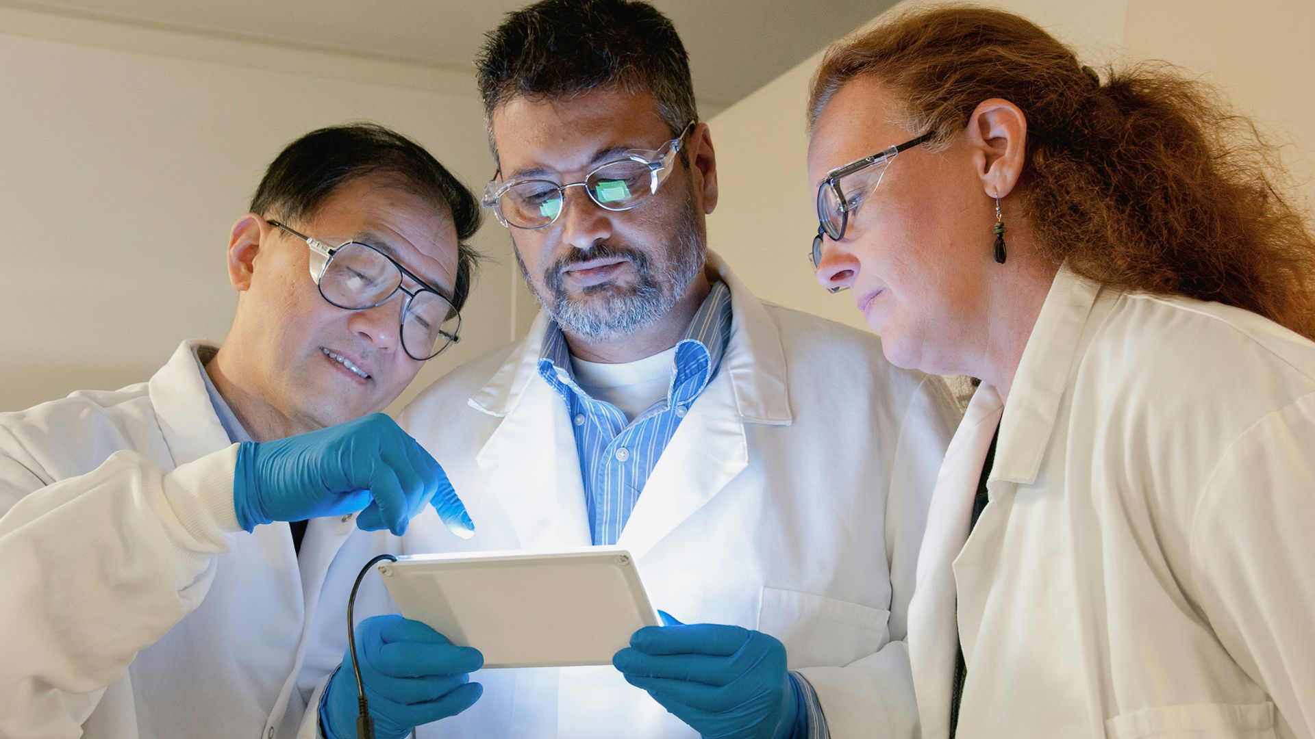 three people in lab coats looking at a tablet