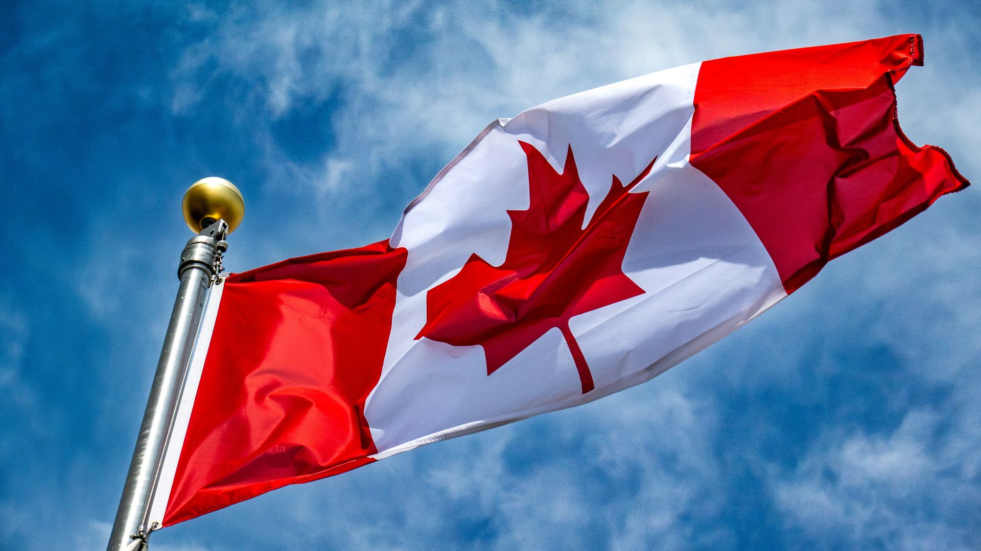 The canadian flag waves proudly against the sky.