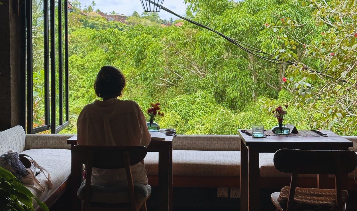 Woman enjoying peaceful moment in indoor cafe with open view to tropical trees in Bali