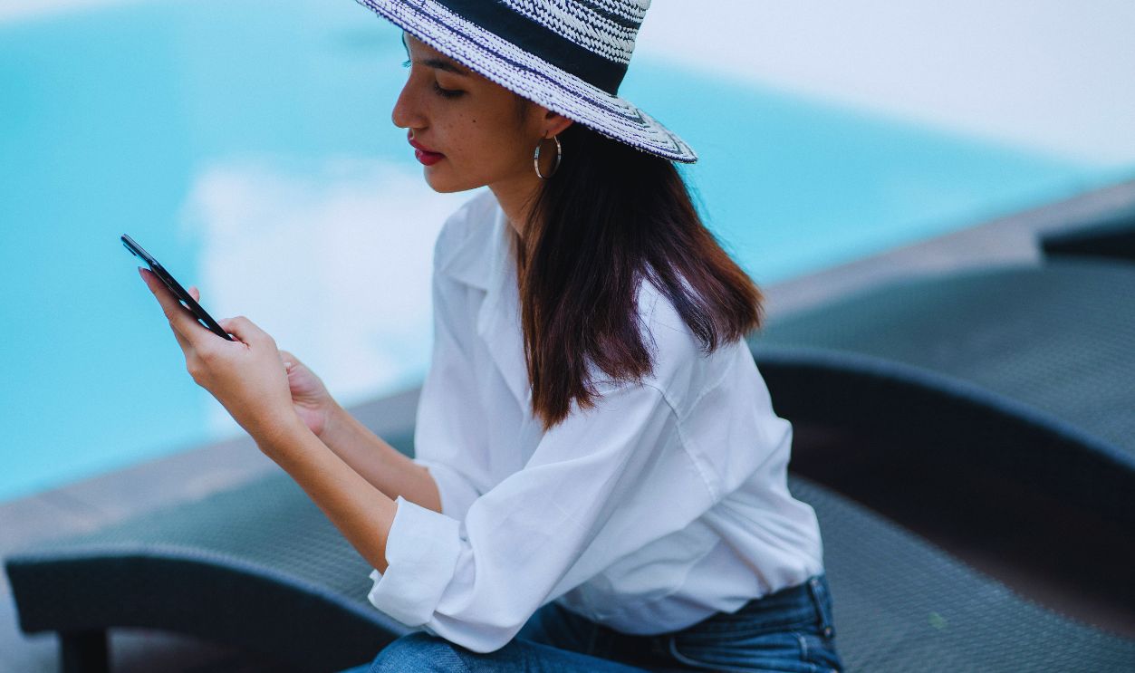 A stylish woman in a straw hat enjoys a sunny day by the pool, using her smartphone