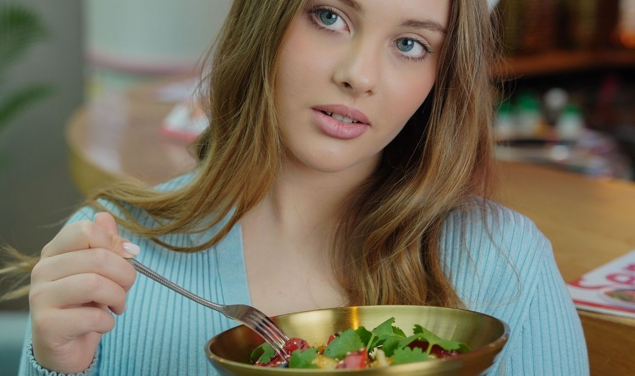 Blonde woman with long hair eating a nutritious salad in a stylish cafe setting